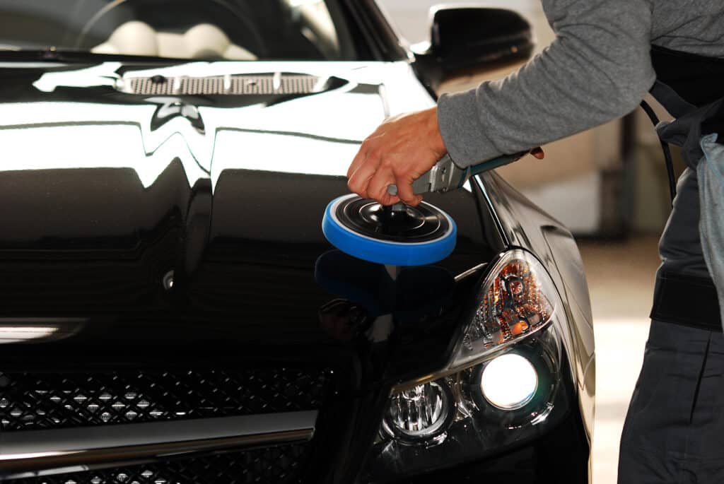 Polissage auto professionnel sur peinture noire brillante Détail d'un homme effectuant un polissage de la peinture noire brillante d'une voiture avec une polisseuse orbitale munie d'un pad bleu.